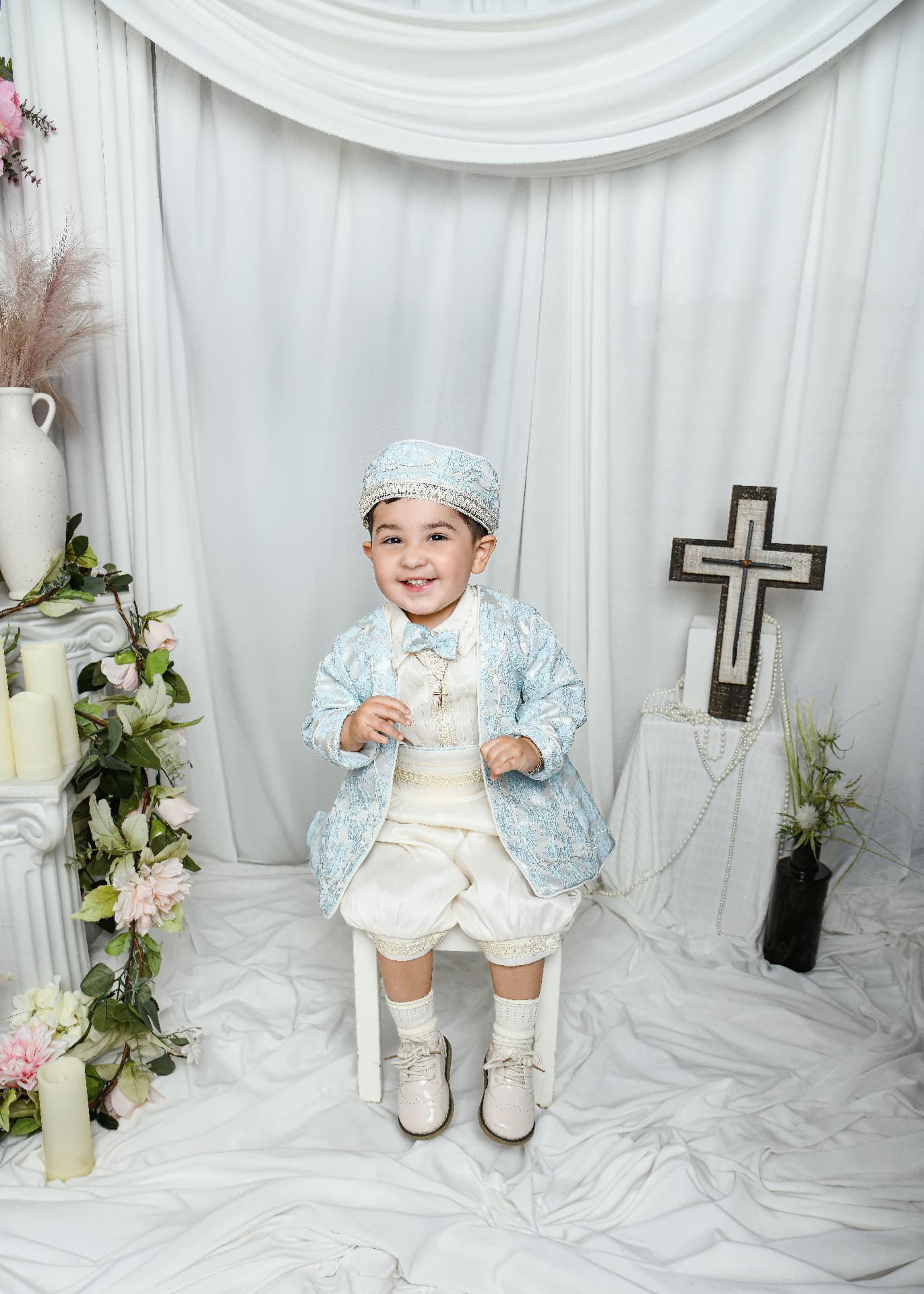 Smiling toddler in a blue baptism suit seated on a white stool