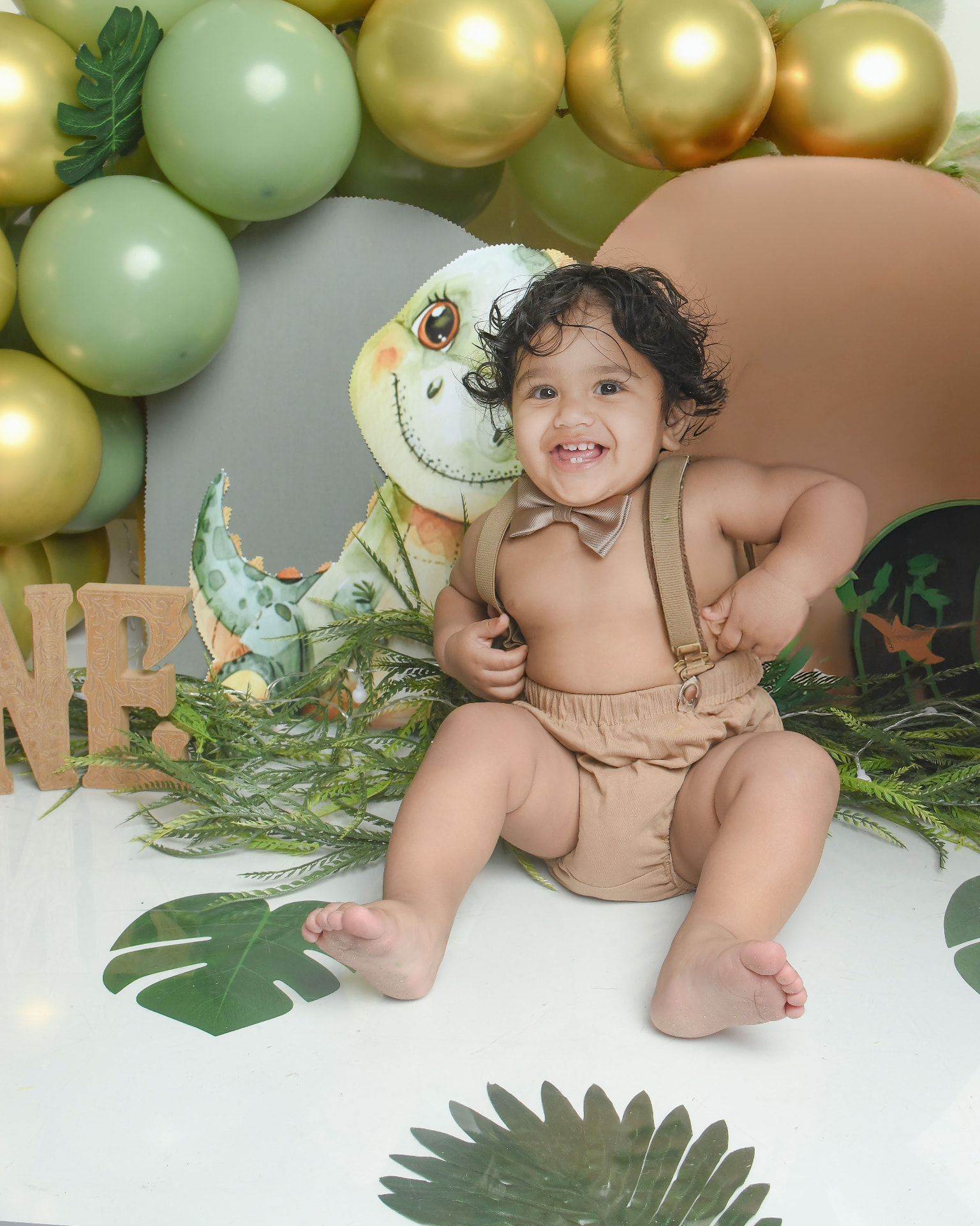 One year old smiling on a dinosaur themed first birthday set