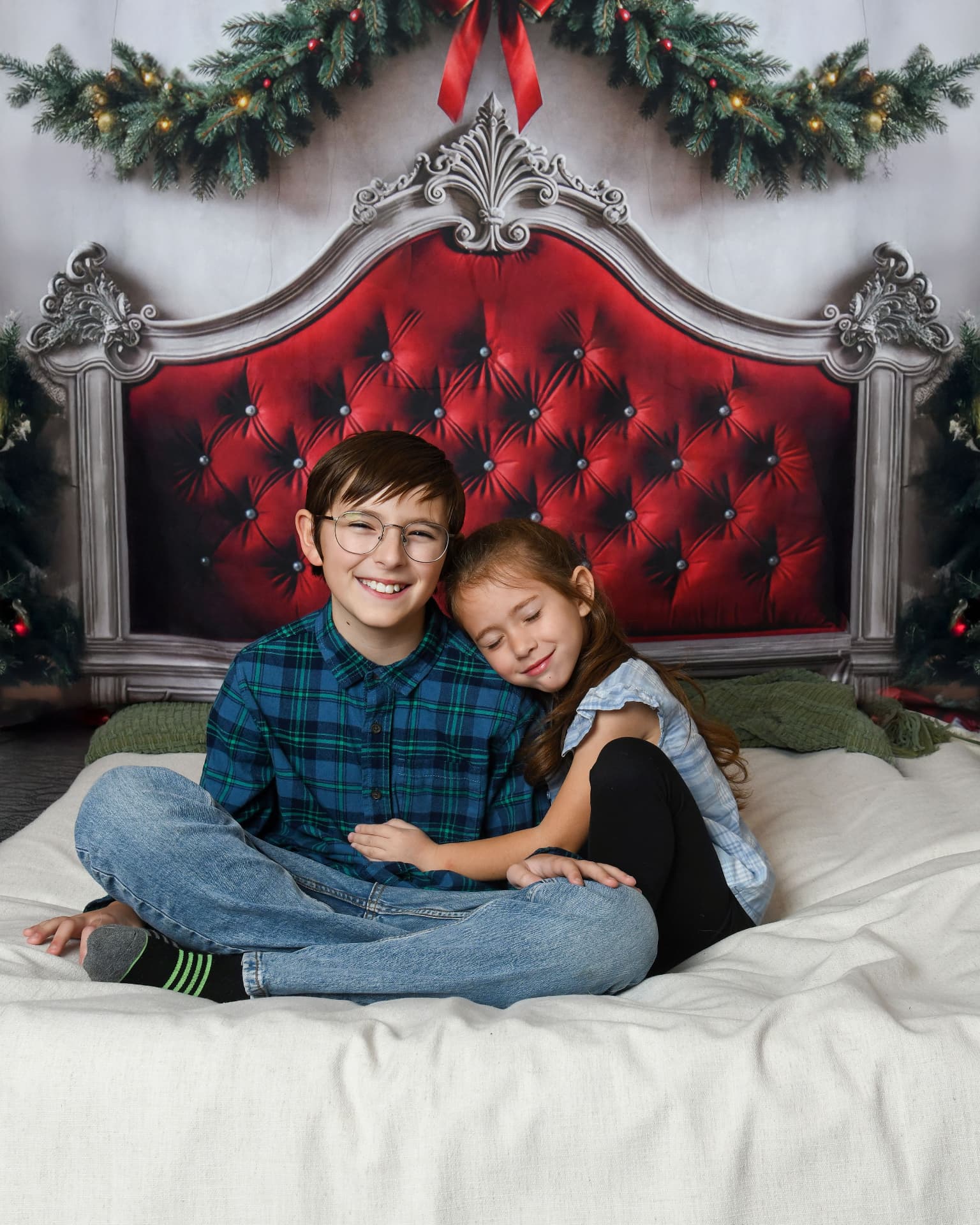Brother and sister cuddling on a holiday set with a red tufted headboard
