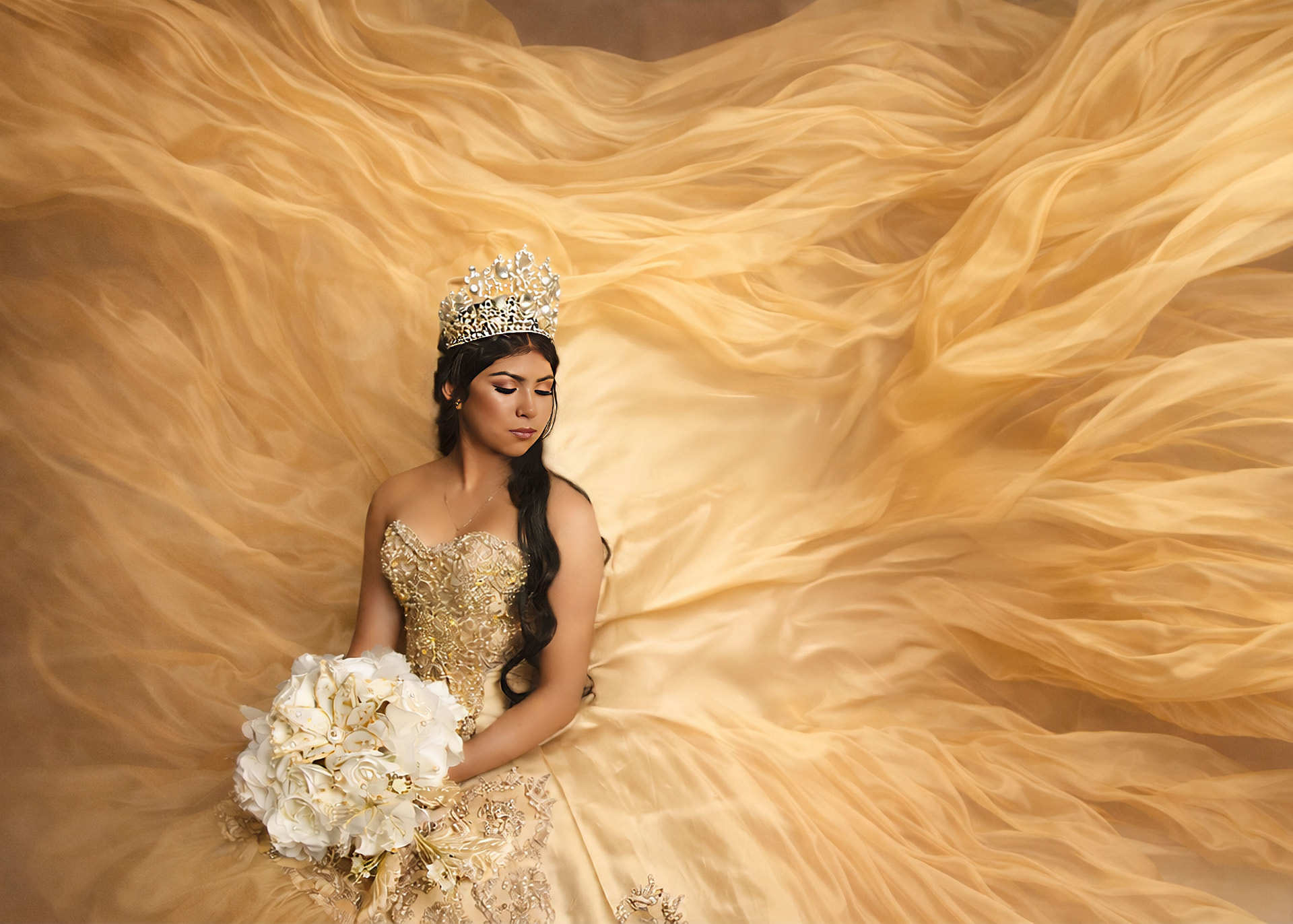 Young woman in an elegant gold quinceañera gown with a crown and white bouquet