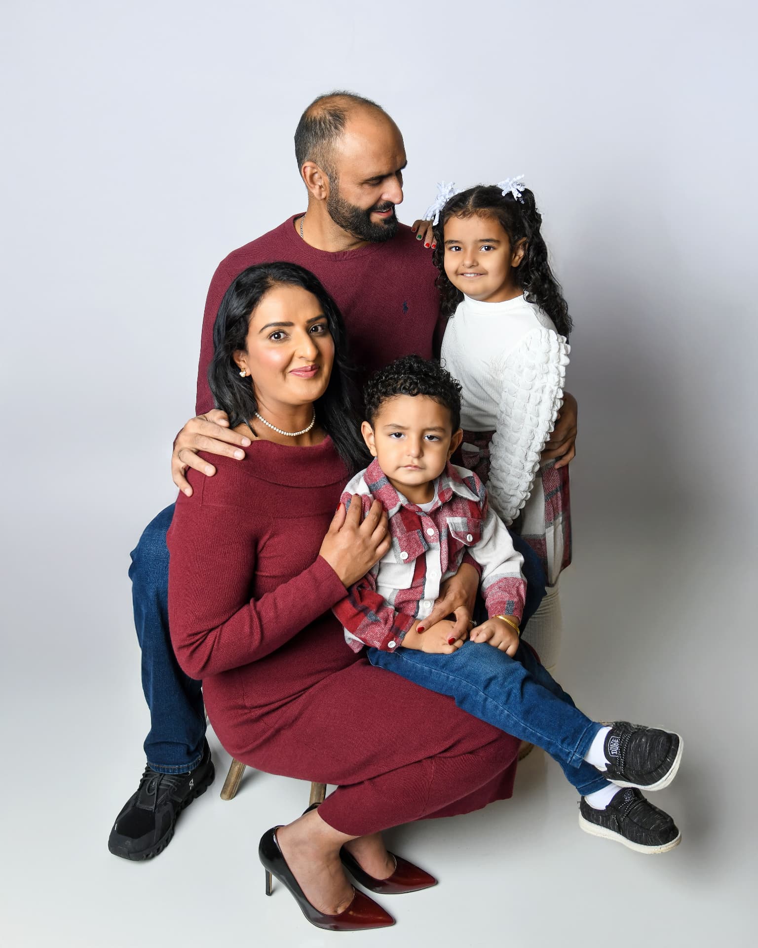 Family of four in burgundy outfits in a clean studio holiday portrait