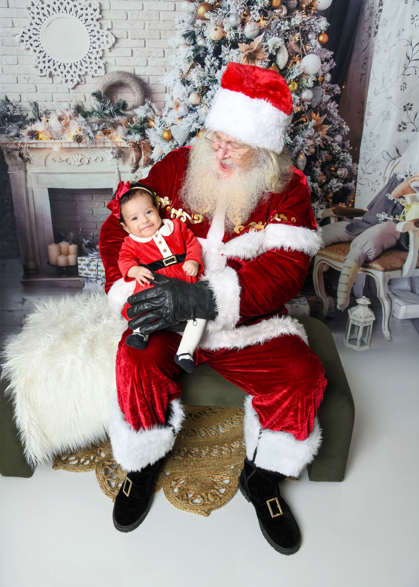 Baby in a Santa suit sitting on Santa's lap in a festive Christmas studio set